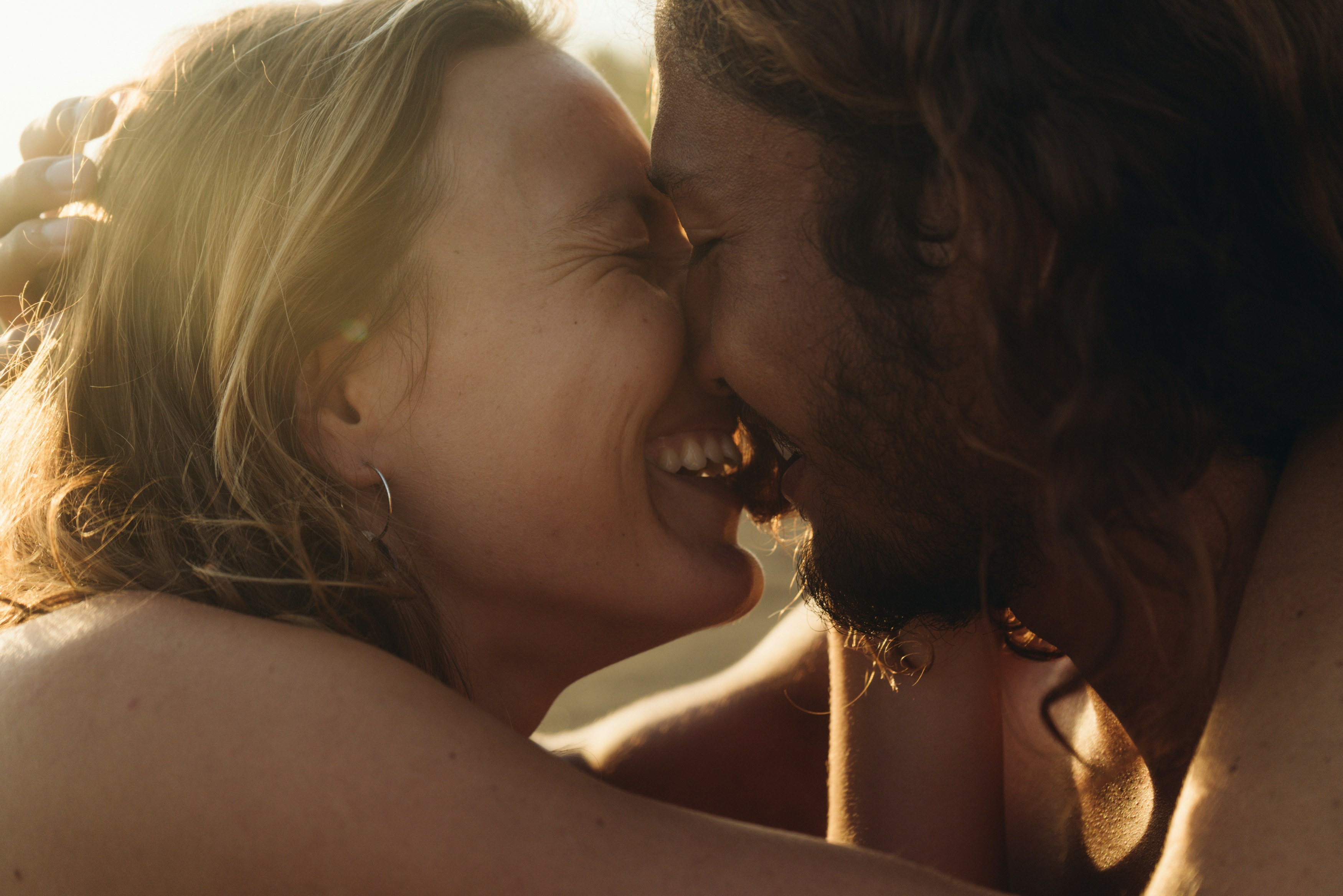 Kissing international couple close-up. Man and woman laugh and touch each other's faces. Sunset time, bright emotions and pure love